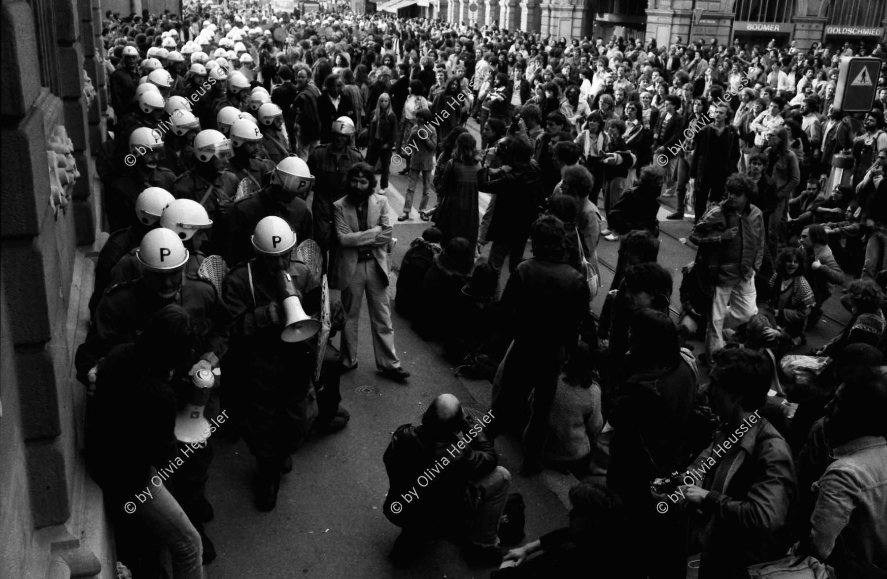 Image of sheet 19800160 photo 29: Demonstrierende versammeln sich vor dem Rathaus: Sie fordern den Gemeinderat zu einer Diskussion auf. Der Gemeinderat verweigert das Gespräch. Die Demonstrierenden harren aus, worauf die Polizei eingreift. 
Zur Forderung eines Autonomen Jugendhauses wird der Platz vor dem Rathaus am Limmatquai besetzt. Sit-In Megaphon mit Bewegungs Sticker. Polizei Einsatz. Polizeihelme von oben herab. 

Jugendbewegung Bewegig AJZ Zürcher Jugendunruhen Demonstrationen
Zürich Protest Youth movement 1980 √