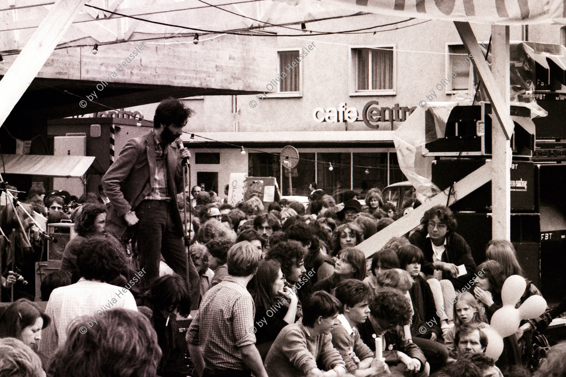 Image of sheet 19800180 photo 18: Klaus Rosza als Redner am Poch Fest Helvetiaplatz. Koni Frei im Publikum. 21.6.1980 Nachdem die rund 5000 bis 6000 auf dem Helvetiaplatz Versammelten von den Präventiv-Verhaftungen vom Freitag erfahren, beschliesst eine Mehrheit, die Diskussion um die von der SP unterbreiteten Vorschläge bezüglich Trägerschaft zu vertagen und stattdessen sofort zu demonstrieren. 
Jugendbewegung Bewegig AJZ Zürcher Jugendunruhen Demonstrationen
Zürich youth movement 1980 √ Kreis 4 vier Aussersihl