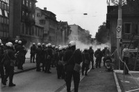 Image of sheet 19800301 photo 18: Vor dem AJZ versammeln sich rund 200 Personen, um für die Einstellung der Strafverfahren zu demonstrieren. Der unbewilligte Demonstrationszug wird von der Polizei aufgelöst: Massive Auseinandersetzungen zwischen den Bewegten und der Polizei, die bis am Sonntagmorgen andauern. Mehr als hundert Personen werden verhaftet. In der folgenden Woche wird in den Medien über das polizeiliche Vorgehen heftig diskutiert.
Das Autonome Jugendzentrum wird ganz mit Tränengas eingeräuchert. Leute kriegen Panik und flüchten auf Dach des AJZ Nach einer Besammlung vor dem AJZ für Demo gegen Isolationshaft greifen Polizeigrenadiere die Leute mit Tränengas Einsatz an. durch Tränengasnebel. 
Jugendbewegung Bewegig AJZ Zürcher Jugendunruhen Demonstrationen
Zürich youth movement protest 1980 √