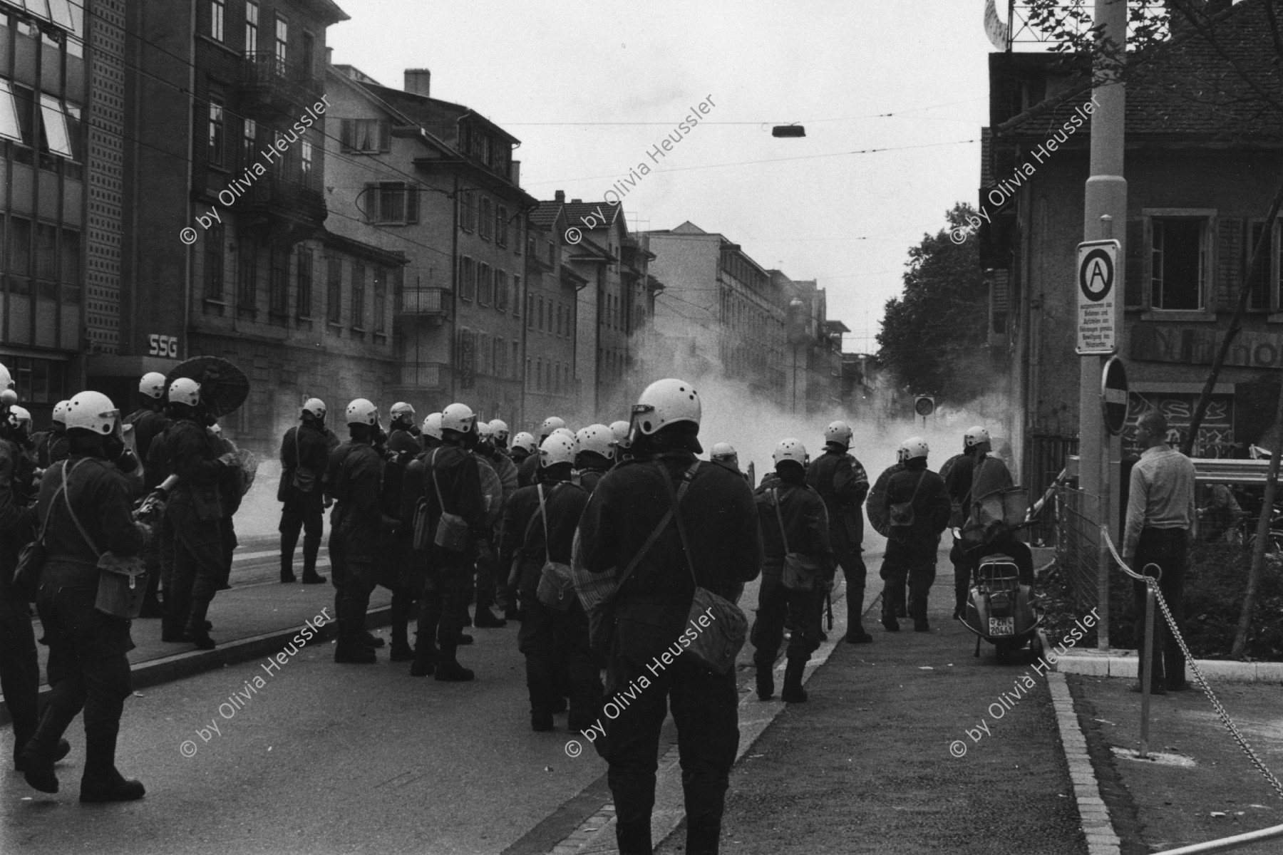 Image of sheet 19800301 photo 18: Vor dem AJZ versammeln sich rund 200 Personen, um für die Einstellung der Strafverfahren zu demonstrieren. Der unbewilligte Demonstrationszug wird von der Polizei aufgelöst: Massive Auseinandersetzungen zwischen den Bewegten und der Polizei, die bis am Sonntagmorgen andauern. Mehr als hundert Personen werden verhaftet. In der folgenden Woche wird in den Medien über das polizeiliche Vorgehen heftig diskutiert.
Das Autonome Jugendzentrum wird ganz mit Tränengas eingeräuchert. Leute kriegen Panik und flüchten auf Dach des AJZ Nach einer Besammlung vor dem AJZ für Demo gegen Isolationshaft greifen Polizeigrenadiere die Leute mit Tränengas Einsatz an. durch Tränengasnebel. 
Jugendbewegung Bewegig AJZ Zürcher Jugendunruhen Demonstrationen
Zürich youth movement protest 1980 √