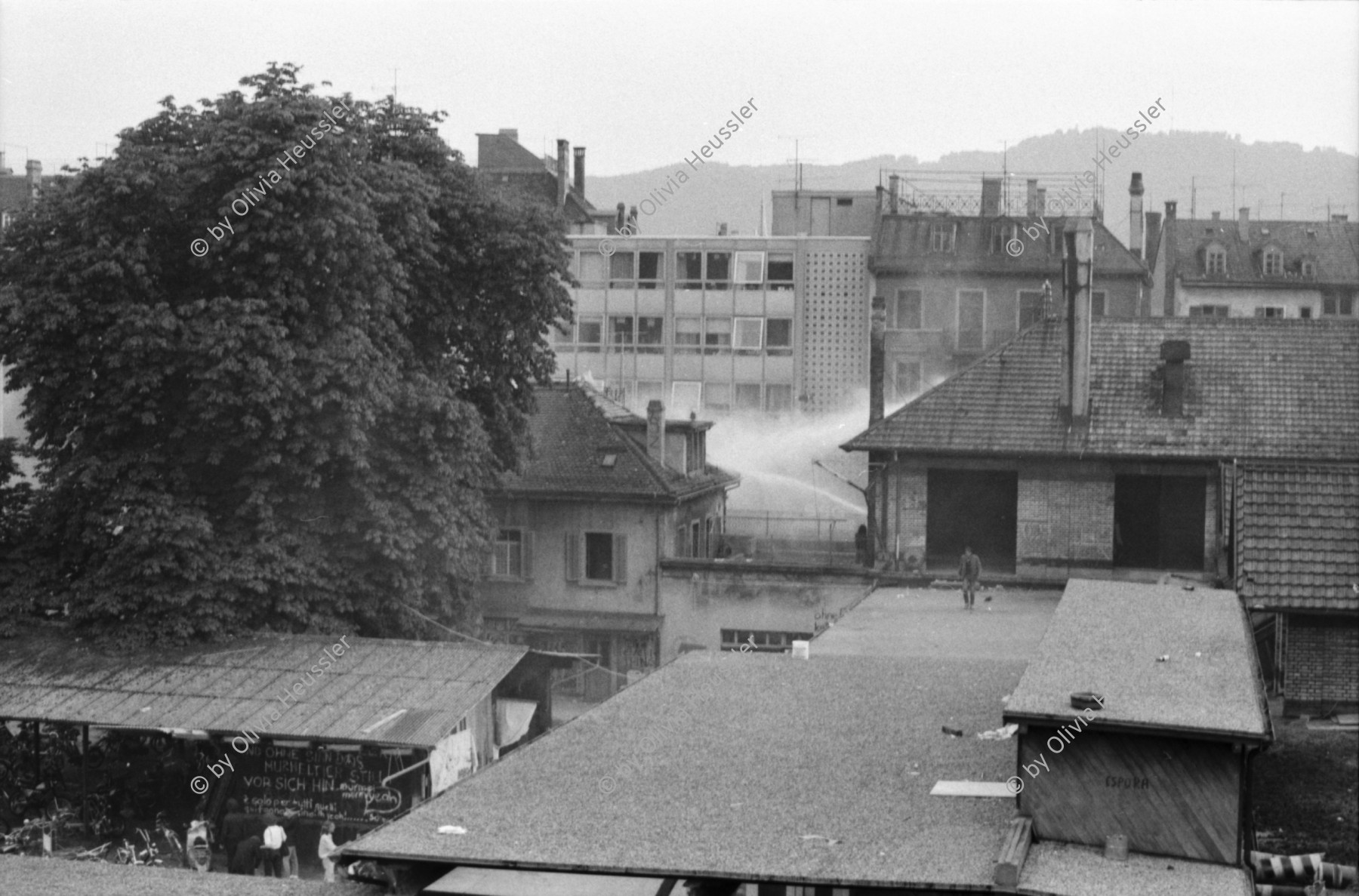 Image of sheet 19800305 photo 10: Vor dem AJZ versammeln sich rund 200 Personen, um für die Einstellung der Strafverfahren zu demonstrieren. Der unbewilligte Demonstrationszug wird von der Polizei aufgelöst: Massive Auseinandersetzungen zwischen den Bewegten und der Polizei, die bis am Sonntagmorgen andauern. 124 Personen werden verhaftet. In der folgenden Woche wird in den Medien über das polizeiliche Vorgehen heftig diskutiert. 
12 Stunden Demonstration. Das AJZ ist vollständig mit Tränengas und Rauch eingehüllt. Auf dem Dach flüchten Leute, die direkt angespritzt werden aus dem Wasserwerfer mit Tränengas Gemisch. Verletzter wird weggetragen. Leute wollen vom Dach springen.
Jugendbewegung Bewegig Zürcher Jugendunruhen Demonstrationen
Zürich youth movement protest 1980 teargas police panic Limmatstrasse Kreis fünf Schweiz Switzerland Europe