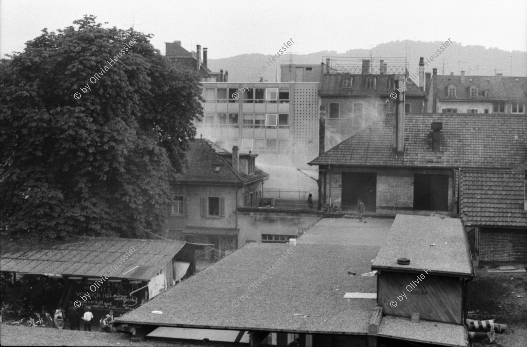 Image of sheet 19800305 photo 9: Vor dem AJZ versammeln sich rund 200 Personen, um für die Einstellung der Strafverfahren zu demonstrieren. Der unbewilligte Demonstrationszug wird von der Polizei aufgelöst: Massive Auseinandersetzungen zwischen den Bewegten und der Polizei, die bis am Sonntagmorgen andauern. 124 Personen werden verhaftet. In der folgenden Woche wird in den Medien über das polizeiliche Vorgehen heftig diskutiert. 
12 Stunden Demonstration. Das AJZ ist vollständig mit Tränengas und Rauch eingehüllt. Auf dem Dach flüchten Leute, die direkt angespritzt werden aus dem Wasserwerfer mit Tränengas Gemisch. Verletzter wird weggetragen. Leute wollen vom Dach springen.
Jugendbewegung Bewegig Zürcher Jugendunruhen Demonstrationen
Zürich youth movement protest 1980 teargas police panic Limmatstrasse Kreis fünf Schweiz Switzerland Europe