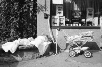 Image of sheet 19800400 photo 1: Kinderwagen  und Spielsachen vor einem Kiosk. Güterwagen überqueren die Strasse.