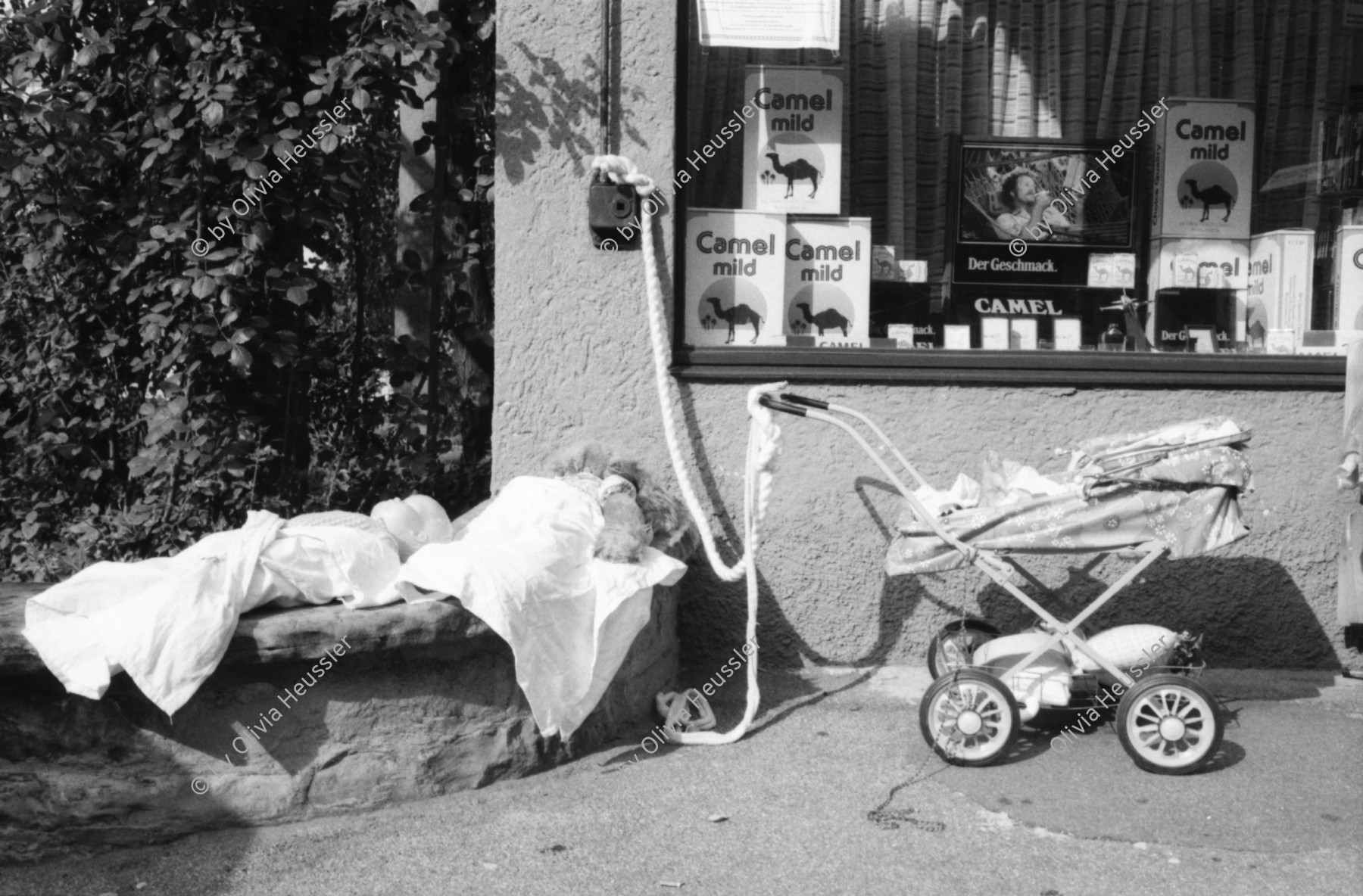 Image of sheet 19800400 photo 1: Kinderwagen  und Spielsachen vor einem Kiosk. Güterwagen überqueren die Strasse.