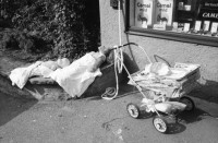 Image of sheet 19800400 photo 2: Kinderwagen  und Spielsachen vor einem Kiosk. Güterwagen überqueren die Strasse.