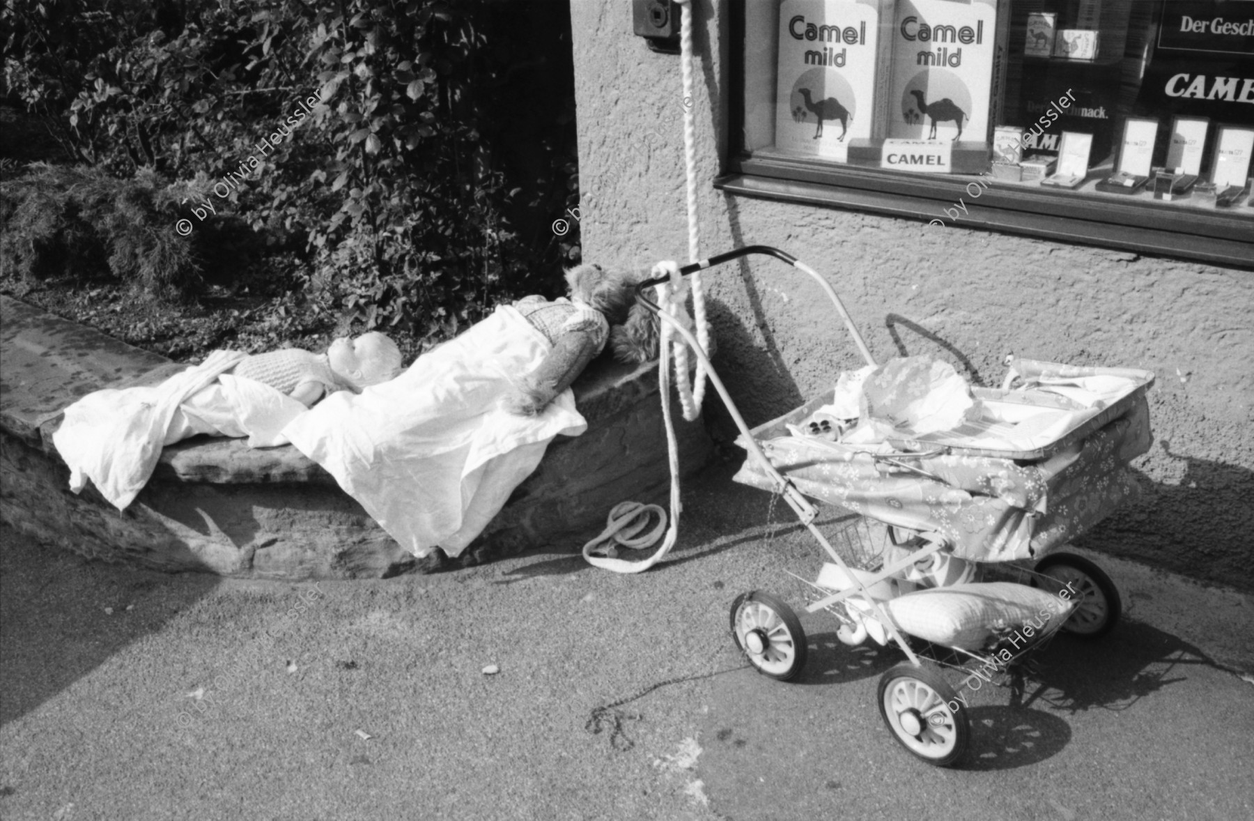 Image of sheet 19800400 photo 2: Kinderwagen  und Spielsachen vor einem Kiosk. Güterwagen überqueren die Strasse.