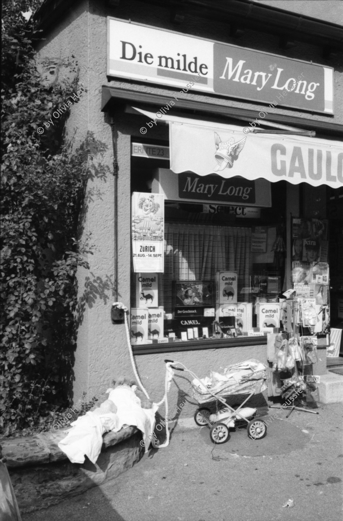 Image of sheet 19800400 photo 3: Kinderwagen  und Spielsachen vor einem Kiosk. Güterwagen überqueren die Strasse.