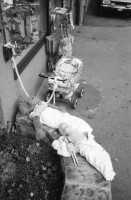Image of sheet 19800400 photo 4: Kinderwagen  und Spielsachen vor einem Kiosk. Güterwagen überqueren die Strasse.