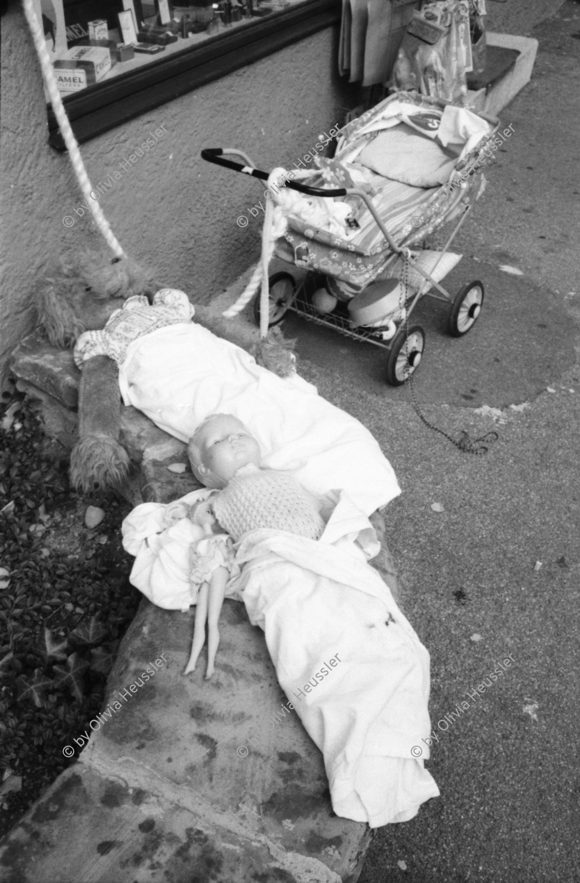 Image of sheet 19800400 photo 6: Kinderwagen  und Spielsachen vor einem Kiosk. Güterwagen überqueren die Strasse.