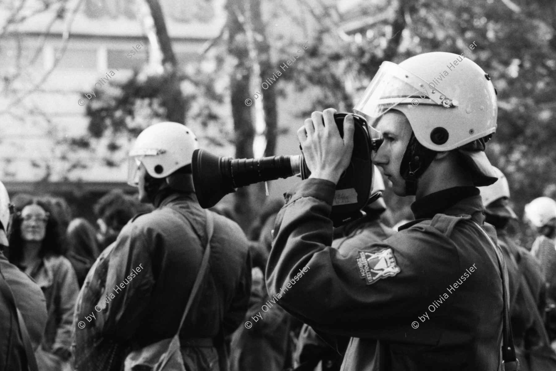 Image of sheet 19800490 photo 33: Auf der Pestalozziwiese findet eine Informationsaktion statt. Die Stadtpolizei lässt die dialogbereiten AJZ-AnhängerInnen, die mit fingierten Auseinandersetzungen ein spontanes Strassentheater mit gemimten PolizistInnen inszenieren, nicht gewähren und verhaftet 144 Personen. Nachdem diese Aktion durch die neue Einkreistaktik der Polizei verhindert worden ist, machen sich in den gemässigten Kreisen der Bewegung Resignation, Enttäuschung und Verzweiflung breit. Polizeibeamte filmt. Film Kamera 

Informationsaktionen: Flugblätter, Strassentheater, Nach Polizeitheater an der siehe Dias, an der Bahnhofstrasse vor dem Globus und auf der Pestalozziwiese werden unter dem Pestalozzi Denkmal 250 Menschen von Polizei in Zivil und uniformiert zusammengepfercht einzeln kontrolliert, registriert, 144 verhaftet und in Sixpacks abgeführt. 
Jugendbewegung Bewegig AJZ Zürcher Jugendunruhen Demonstrationen

Zürich 1980 youth movement √