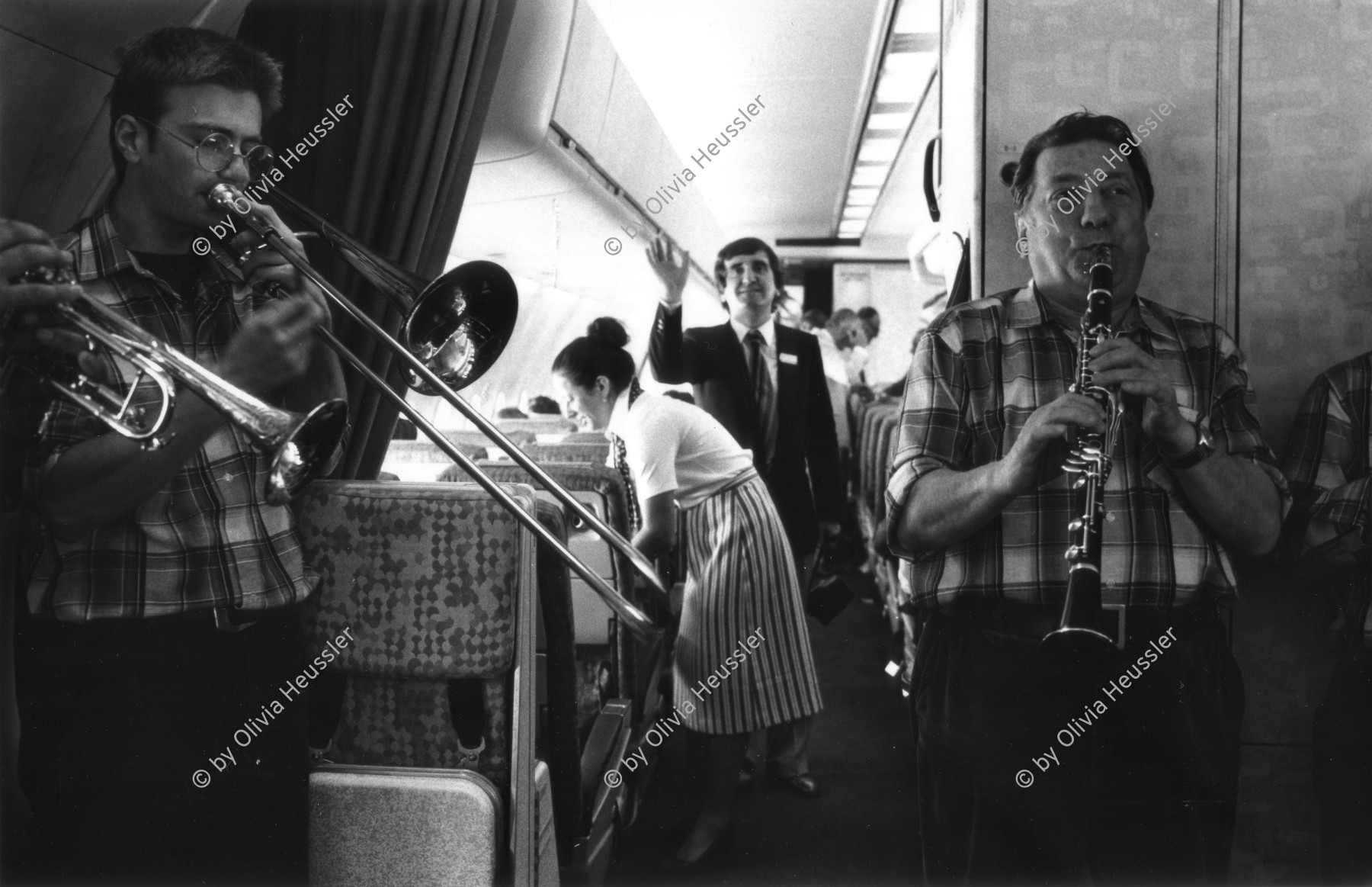 Image of sheet 19810210 photo 34: Im Flughafen Zürich Kloten wird eine DC 10 auf den namen Ticino getauft. Musik wird gespielt auf dem Flug über Nizza und zurück. Piloten stehen da in Gruppen. Im Innern spielen 2 Männer aus einem Tessiner Musik Grüppli Turbine.  Zürich √