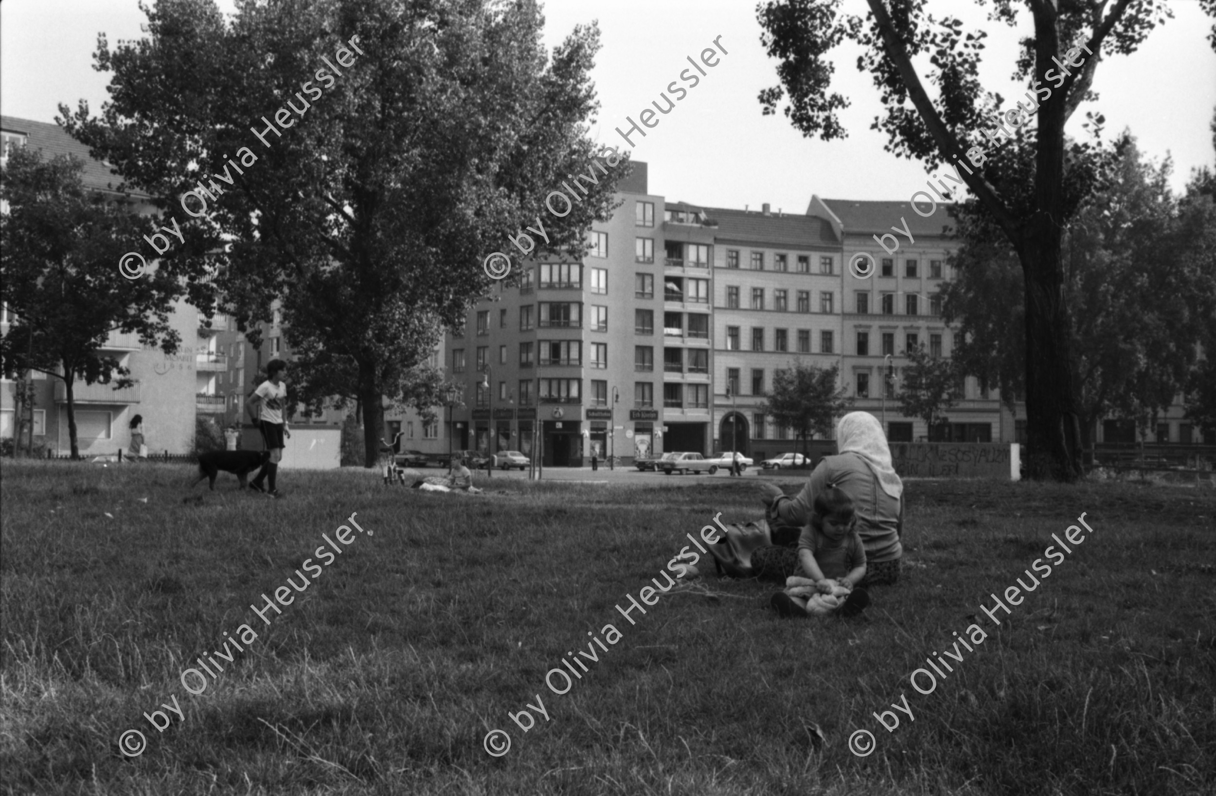 Image of sheet 19810380 photo 11: Häuserfassaden. Türkin sitzt auf Wiese vor Künstlerhaus. X Besetztes Haus. Berlin Westdeutschland 1981 türkische Frau Kopftuch Piknik Bäume Trees Woman turkish Imigrant Germany