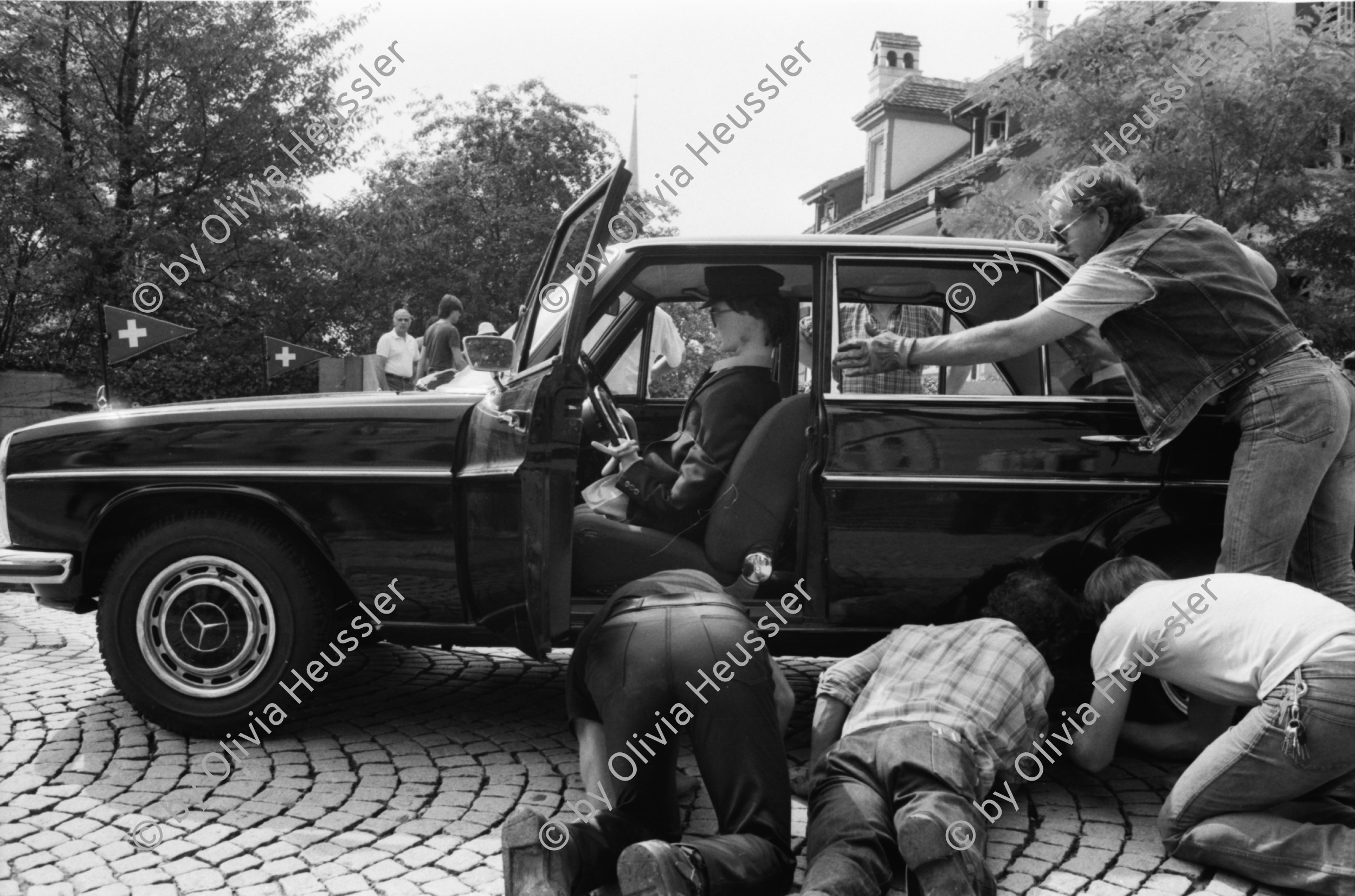 Image of sheet 19810430 photo 25: frtsg 810420 Espion lève-toi. Directed by Yves Boisset. With Lino Ventura, Michel Piccoli, Bruno Cremer. 1981
Polizei Motorrad mit Stilett Sticker Kleber. Puppe Attrappe im Mercedes  Benz Hopi, drei Männer Hinter unter Mercedes liegen Statisten
Zürich 1981 Swiss Schweiz Switzerland Europe cinema french criminal movie france police