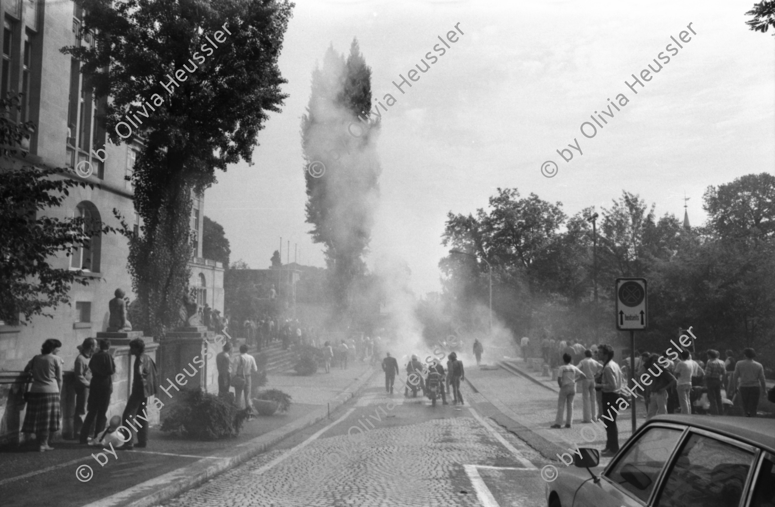 Image of sheet 19810450 photo 19: Drehaufnahmen zum Film Espion leve toi von Yves Poisset 
Männer befestigen Schweizerfähnchen auf Mercedes Benz Universität Zürich
brennt noch Loch im Schlauch der Feuerwehr Rauchfahne
Zürich Künstlergasse 1981