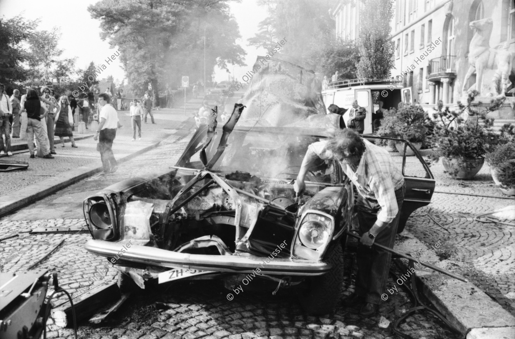 Image of sheet 19810460 photo 12: frstg 810450 Teile vom Mercedes Benz liegen herum Hopi. Polizei auf Motorrad, Der spätere Kunstmaler Aleks Weber mit gebleichtem Haar. Feuerwehr löscht Brand. Yves Poisset Espion l'ève toi. Motorrad fahrer wird von Sanität mit Helm abgeführt. Zürich 1981