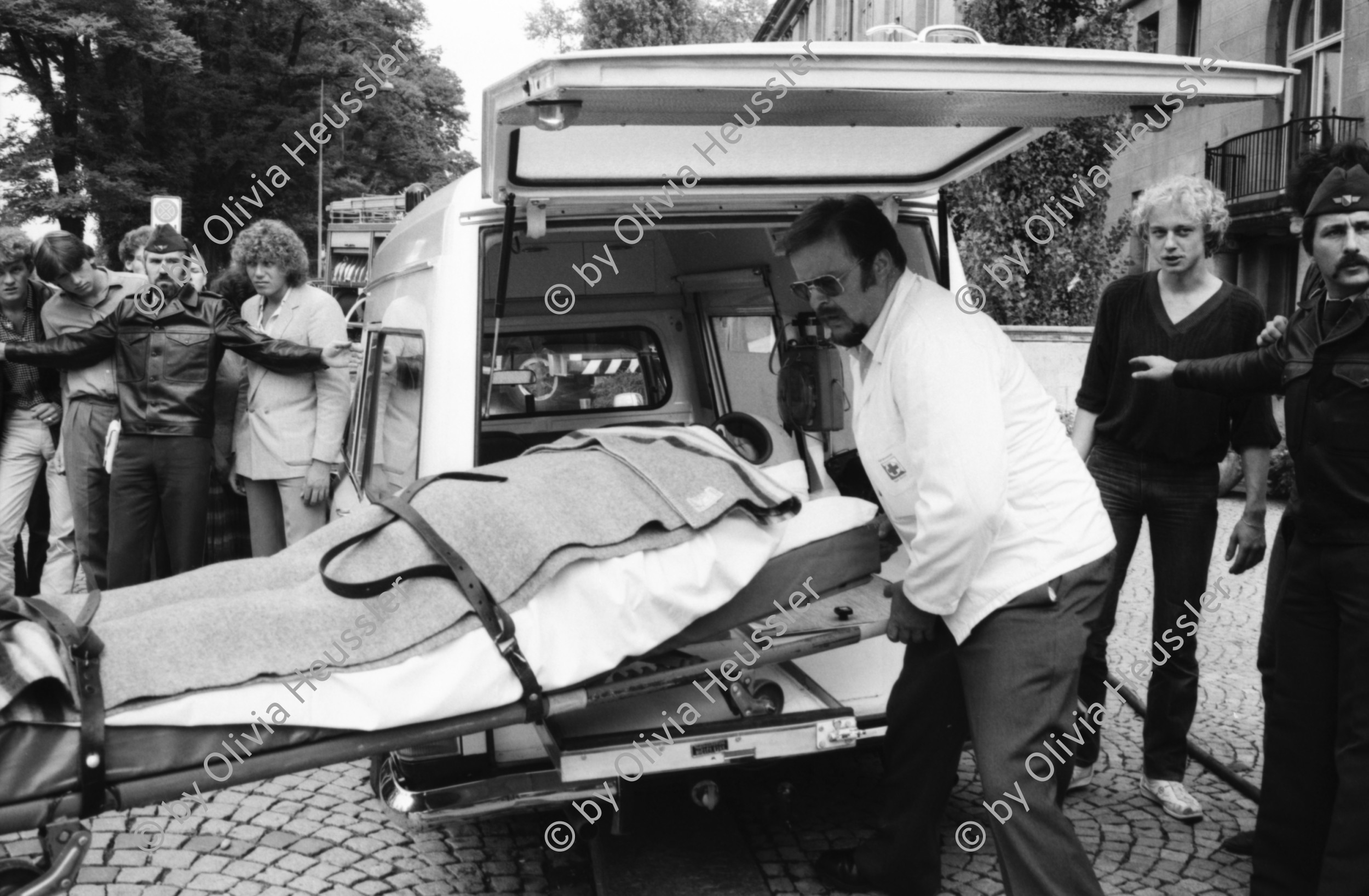 Image of sheet 19810460 photo 35: frstg 810450 Teile vom Mercedes Benz liegen herum Hopi. Polizei auf Motorrad, Der spätere Kunstmaler Aleks Weber mit gebleichtem Haar. Feuerwehr löscht Brand. Yves Poisset Espion l'ève toi. Motorrad fahrer wird von Sanität mit Helm abgeführt. Zürich 1981