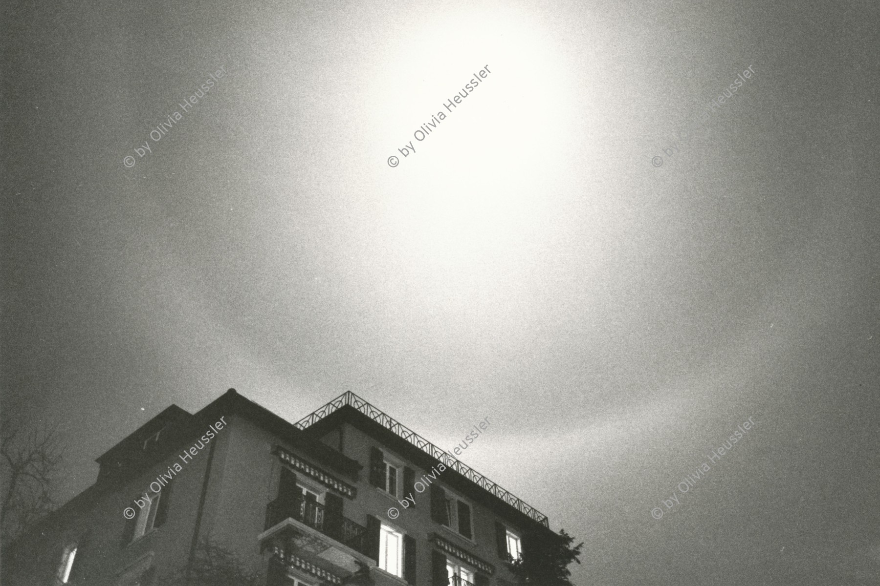 Image of sheet 19820112 photo 13: Lichtkreis um Mond Halo 'Dampfring' Weinbergstrasse 84
Zürich 1982 √

Halo (Singular der Halo; Plural Halos oder Halogone) ist ein Sammelbegriff für Lichteffekte der atmosphärischen Optik, die durch Reflexion und Brechung von Licht an Eiskristallen entstehen.
A 22° halo is a halo, one type of optical phenomenon, forming a circle 22° around the sun, or occasionally the moon. It forms as sunlight is refracted in hexagonal ice crystals suspended in the atmosphere. As the light beam passes through two sides of the prism forming a 60° angle, the angle of minimum deviation is almost 22° (namely, 21.84° on average; 21.54° for red and 22.37° for blue). This wavelength-dependent variation in refraction causes the inner edge of the circle to be reddish while the outer edge is bluish. A 22° halo may be visible on as many as 100 days per year.

copyright by Olivia Heussler