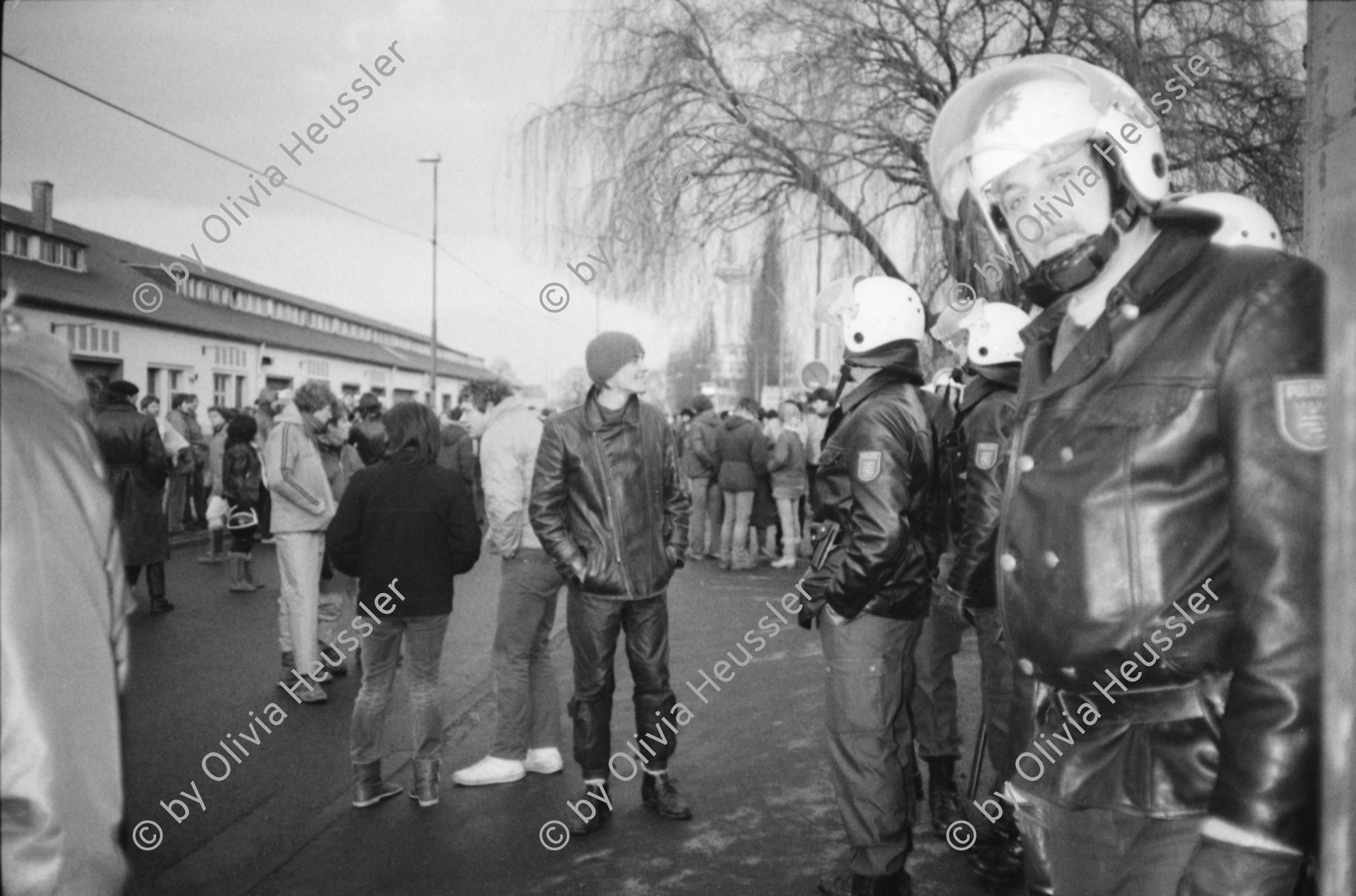 Image of sheet 19830300 photo 1: In Frankfurt Hausen ist eine Blockade gegen die Mittelstreckenraketen Depot im Gang. Die Polizei greift ein. Nachts werden die von der US- Armee bewachten Raketen in Containern weggefahren. Im Convoi fährt ein Rolls Royce 
Käthe Kollwitz Haus Strassentafel Frankfurt a. Main. Germany Deutschland 1983