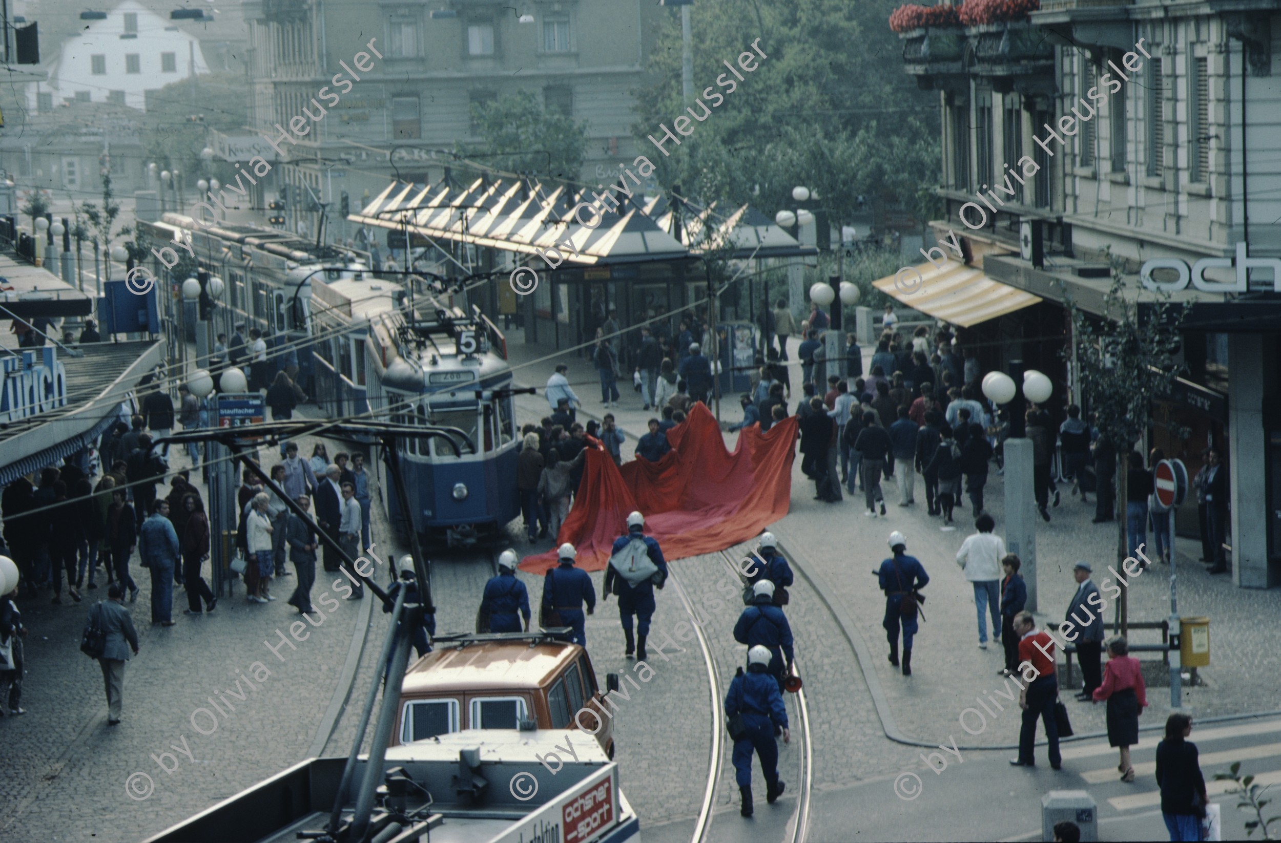 Image of sheet 19833000 photo 15: Am Tor zu Aussersihl
Am Stauffacherplatz Badenerstrasse wird das Eckhaus besetzt. Ein rotes Tuch wird auf den Platz über die Tramschienen der VBZ gelegt. Polizeibeamte nehmen das Tuch auf und die Leute reissen es ihnen aus den Händen. So geht es weiter durch die Stadt. Housing, Besetzung Wohnen, Wohnungsnot, Wohnungsmangel, protest action, art, installation, Stauffacher,  
Zürich Schweiz Switzerland
Exhibition: Zurich, The Eighties Photobastei 2020
»Counter Power« Altkirch 2017 framed pp 40 x 60 cm
