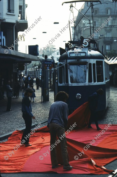 Image of sheet 19833000 photo 17: Am Tor zu Aussersihl
Am Stauffacherplatz Badenerstrasse wird das Eckhaus besetzt. Ein rotes Tuch wird auf den Platz über die Tramschienen der VBZ gelegt. Polizeibeamte nehmen das Tuch auf und die Leute reissen es ihnen aus den Händen. So geht es weiter durch die Stadt. Housing, Besetzung Wohnen, Wohnungsnot, Wohnungsmangel, protest action, art, installation, Stauffacher,  
Zürich Schweiz Switzerland