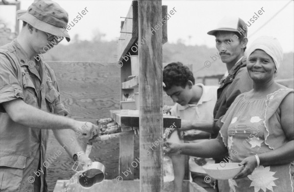 Image of sheet 19840180 photo 8: Helikopter Flugzeug Ausbildung im Schiessen mit amerikanischem Instruktor. US-Army Soldaten in Zivil vor Bar. Junge schleckt US Marmelade aus Dose. Honduranische Polizei. Anit Kommunisten Wandmalerei. Spray Wachturm in Palmerola. Junge und Soldaten. Bahnhof Eisenbahn. Mädchen und Mutter auf dem Weg zur Kirche mit Mais blätter. Lacayo ehem. Nic. Kulturminister und Mann von Anna Qriquillon. Gabriela Battaglia. San Pedro Sula Honduras Mittelamerika Centralamerica 1984