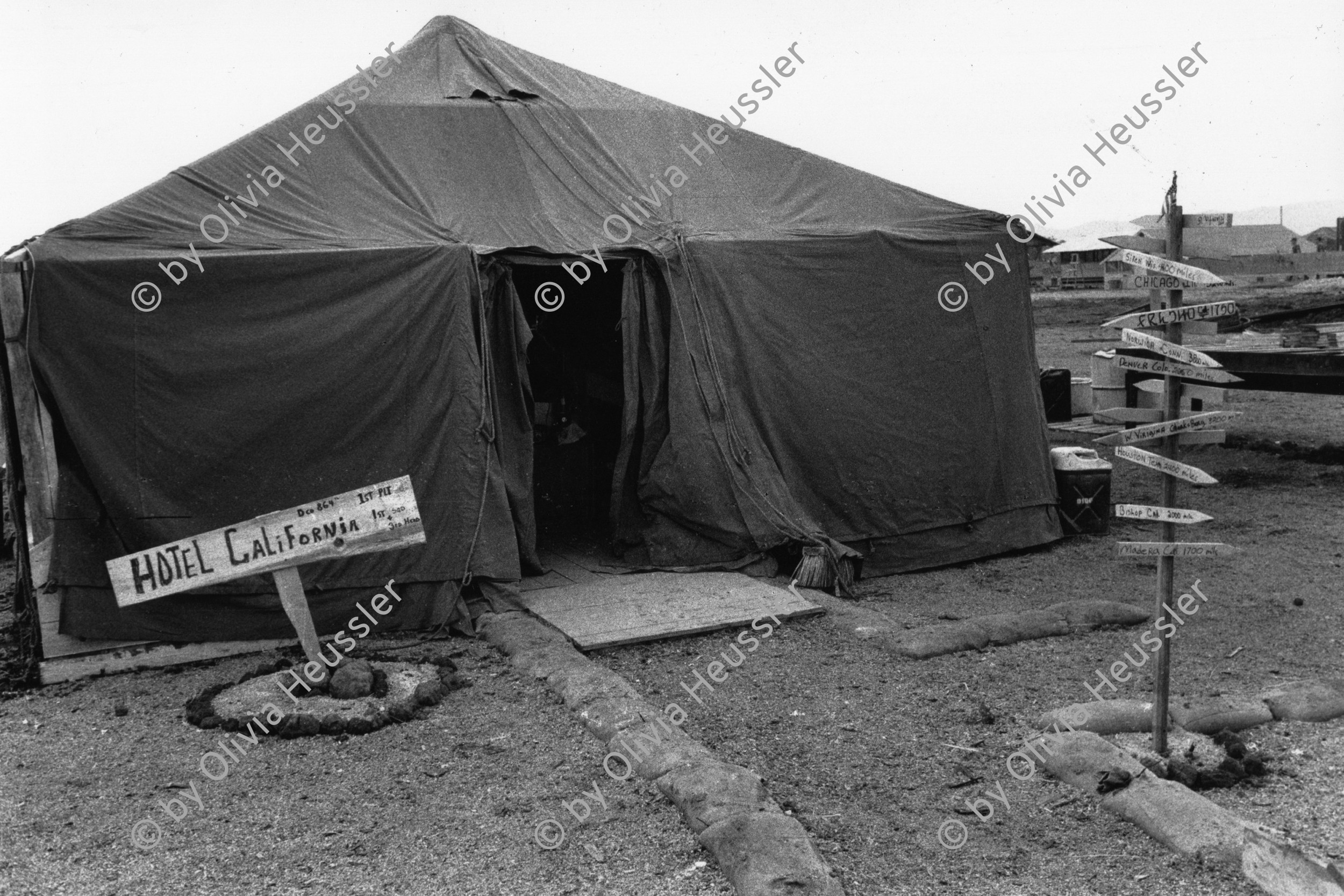 Image of sheet 19840210 photo 37: Das 'Hotel California' dient den US-Soldaten auf der Militärflughafenbase bei Jamastran, in der Nähe der Grenze zu Nicaragua. Danli Honduras 04.84 Zentralamerika Centralamerica 1984 √ soldier army military tent camp us american base airplane airport 




Out of: Der Traum von Solentiname  /  The dream of Solentiname  /  El sueño de Solentiname page 46

Aus: von Zeit zu Zeit Out of: from Time to Time

«Hotel» e indicadores de los lugares de origen de los estadounidenses que
trabajan en la construcción de una pista de aterrizaje en apoyo de la Contra. Jamastrán, Dpto. de El Paraíso, Honduras, 1984.
“Hotel” and signs pointing home for U.S. soldiers building the runway
to supply the Contras. Jamastrán, Dep. El Paraíso
Exhibition