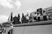 Image of sheet 19840290 photo 16: Geburtstag Sandinos. Des Generals des freien Menschen, wird gefeiert. «Sandino vive» steht an den Mauern. Kinder in Reihe. Gruppenbild. Bühne. FSLN Fahne. Mann Soldat mit Maske. Kommandanten mit Strohhüten. Fahnen. Mascottchen kleines Kind in Uniform. Marimbas werden an der Demo für Sandino mitgetragen. Masken werden getragen. Mural Wandmalerei Ein junger Soldat der den Helikopter abgeschossen hat mit den Honduranern drin. Nicaragua 1984