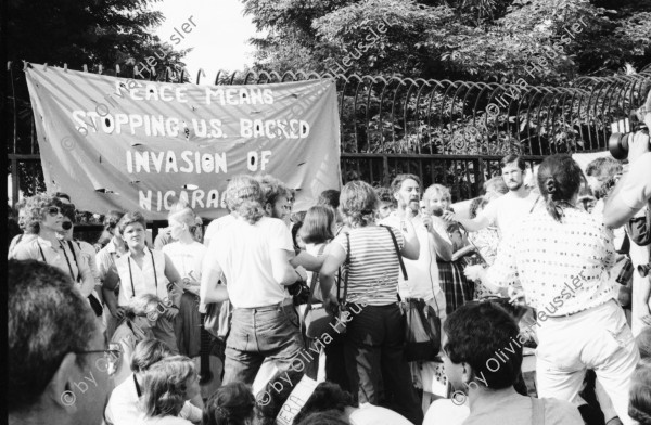 Image of sheet 19840410 photo 19: Viele Nordamerikaner Innen demonstrieren vor ihrer Botschaft. Protest US Amerikaner innen. U.S.A. Portrai Frau mit hut. Die Fahne weht auch stolz über ihr. Peace means stoping US backed Invasion of Nicaragua. Marsch am 19.Juli auf der Carretera Norte, vorbei an den Texnicsa. Wandbild mit Sandino.