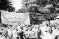 Image of sheet 19840410 photo 20: Viele Nordamerikaner Innen demonstrieren vor ihrer Botschaft. Protest US Amerikaner innen. U.S.A. Portrai Frau mit hut. Die Fahne weht auch stolz über ihr. Peace means stoping US backed Invasion of Nicaragua. Marsch am 19.Juli auf der Carretera Norte, vorbei an den Texnicsa. Wandbild mit Sandino.