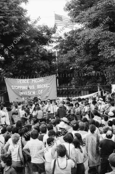 Image of sheet 19840410 photo 25: Viele Nordamerikaner Innen demonstrieren vor ihrer Botschaft. Protest US Amerikaner innen. U.S.A. Portrai Frau mit hut. Die Fahne weht auch stolz über ihr. Peace means stoping US backed Invasion of Nicaragua. Marsch am 19.Juli auf der Carretera Norte, vorbei an den Texnicsa. Wandbild mit Sandino.