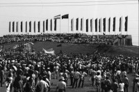 Image of sheet 19840420 photo 14: Todo para los frente de Guerra. Todo para los Combatientes. Am 5. Jahrestag der Revolution festen auch die Fabriken an der Carretera Norte. Fabrikarbeiter. Sicht durch die Ruinen aufs Gebäude der Banco de America. Im Vordergrund Demonstration. Die Fahnen wehen für die Revolution auf dem Platz. Das Nic. Rote Kreuz verteilt den erhitzten Köpfen Trinkwasser. Erdbebenruinen. Managua 1984