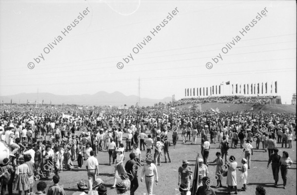 Image of sheet 19840420 photo 15: Todo para los frente de Guerra. Todo para los Combatientes. Am 5. Jahrestag der Revolution festen auch die Fabriken an der Carretera Norte. Fabrikarbeiter. Sicht durch die Ruinen aufs Gebäude der Banco de America. Im Vordergrund Demonstration. Die Fahnen wehen für die Revolution auf dem Platz. Das Nic. Rote Kreuz verteilt den erhitzten Köpfen Trinkwasser. Erdbebenruinen. Managua 1984