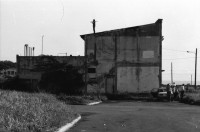 Image of sheet 19840420 photo 5: Todo para los frente de Guerra. Todo para los Combatientes. Am 5. Jahrestag der Revolution festen auch die Fabriken an der Carretera Norte. Fabrikarbeiter. Sicht durch die Ruinen aufs Gebäude der Banco de America. Im Vordergrund Demonstration. Die Fahnen wehen für die Revolution auf dem Platz. Das Nic. Rote Kreuz verteilt den erhitzten Köpfen Trinkwasser. Erdbebenruinen. Managua 1984