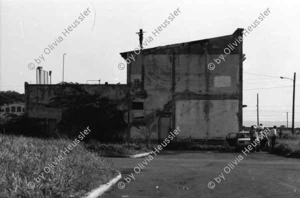 Image of sheet 19840420 photo 5: Todo para los frente de Guerra. Todo para los Combatientes. Am 5. Jahrestag der Revolution festen auch die Fabriken an der Carretera Norte. Fabrikarbeiter. Sicht durch die Ruinen aufs Gebäude der Banco de America. Im Vordergrund Demonstration. Die Fahnen wehen für die Revolution auf dem Platz. Das Nic. Rote Kreuz verteilt den erhitzten Köpfen Trinkwasser. Erdbebenruinen. Managua 1984