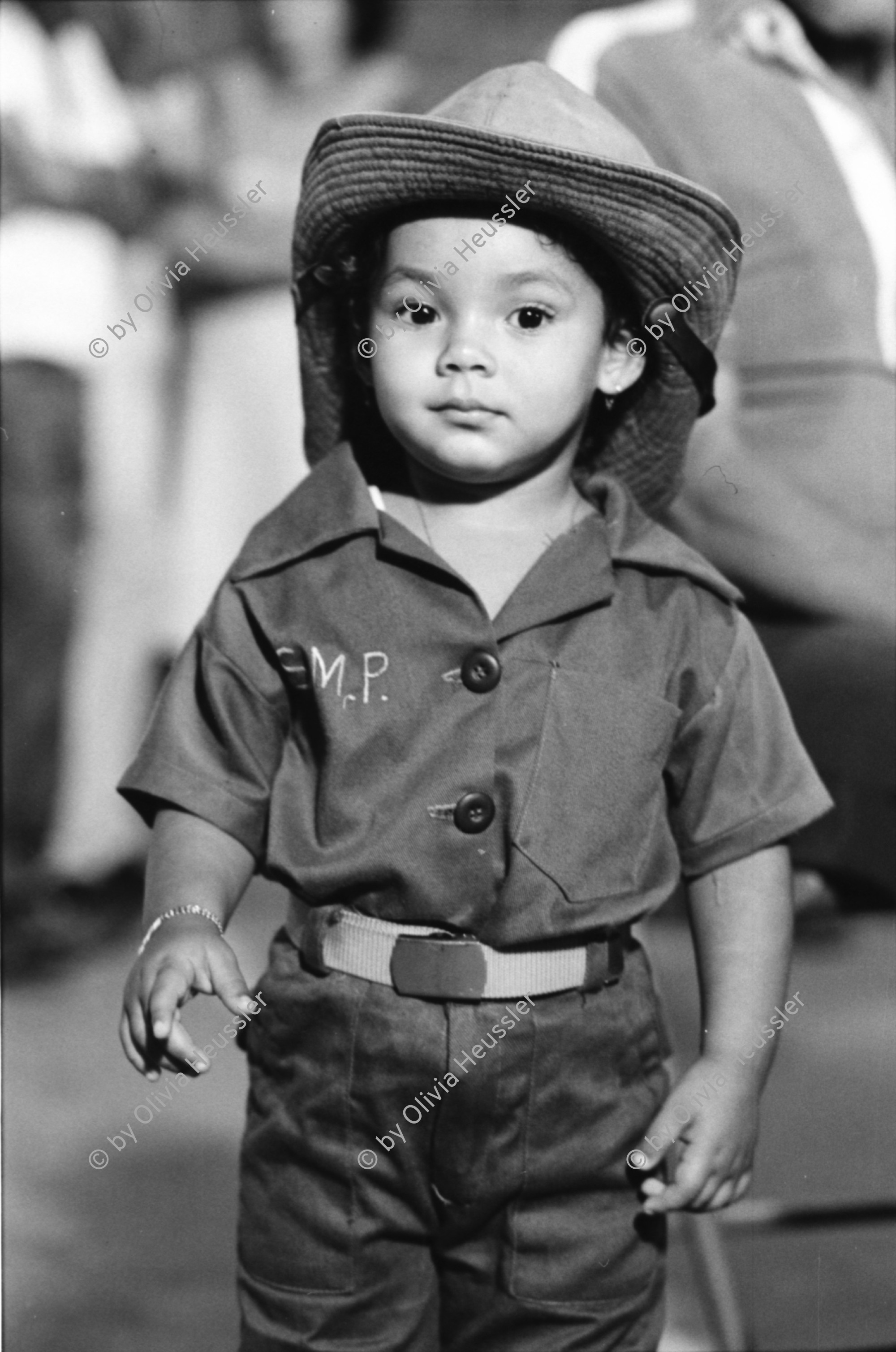 Image of sheet 19840500 photo 34: Majorettes treten für Daniel Ortega auf. Kindergruppe. Kirche von Bluefields. Esso Tankstelle. kleine Fischerboote im Hafen von B-. Palmen. Kinder vor Wandmalerei. Mascotta. kleines Mädchen als Kindersoldat verkleidet. S.M.P. Servicio Militar Patriotico. Tafel des P.L.I. in Managua. Partido Liberal Independiente. Atlantikküste RAAS 1984