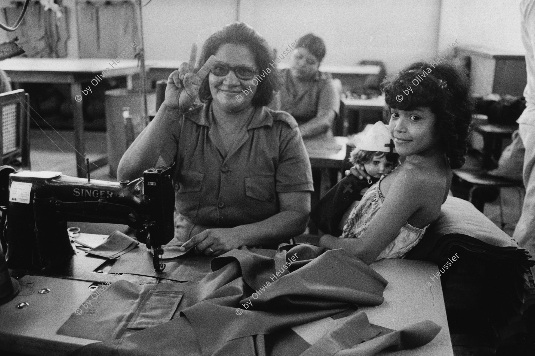 Image of sheet 19840560 photo 15: In einer Schneiderei der sandinistischen Armee arbeiten viele Frauen an der Nähmaschine. Sie machen die Uniformen für die Armee. FSLN Ihre Kinder begleiten sie, im Mangel an Tagesschulen. Managua Nicaragua. 1984 √