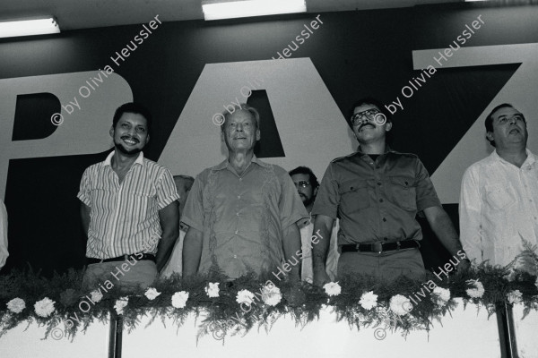 Image of sheet 19840600 photo 16: Aus: «Der Traum von Solentiname» EPF, Zürich 
«El Sueño de Solentiname» IHNCA Managua p.54 oben

German Federal Chancellor and Social Democrat Willy Brandt is awarded an honorary degree of the Universidad Nacional Autónoma de Nicaragua (UNAN ) by revolutionary commanders Bayardo Arce (l.) and Daniel Ortega (r.). Managua, 1984

Der deutsche Bundeskanzler und Sozialdemokrat Willy Brandt erhält von Revolutionskommandanten Bayardo Arce (l.) und Daniel Ortega (r.) den Ehrendoktor der Universidad Nacional Autónoma de Nicaragua