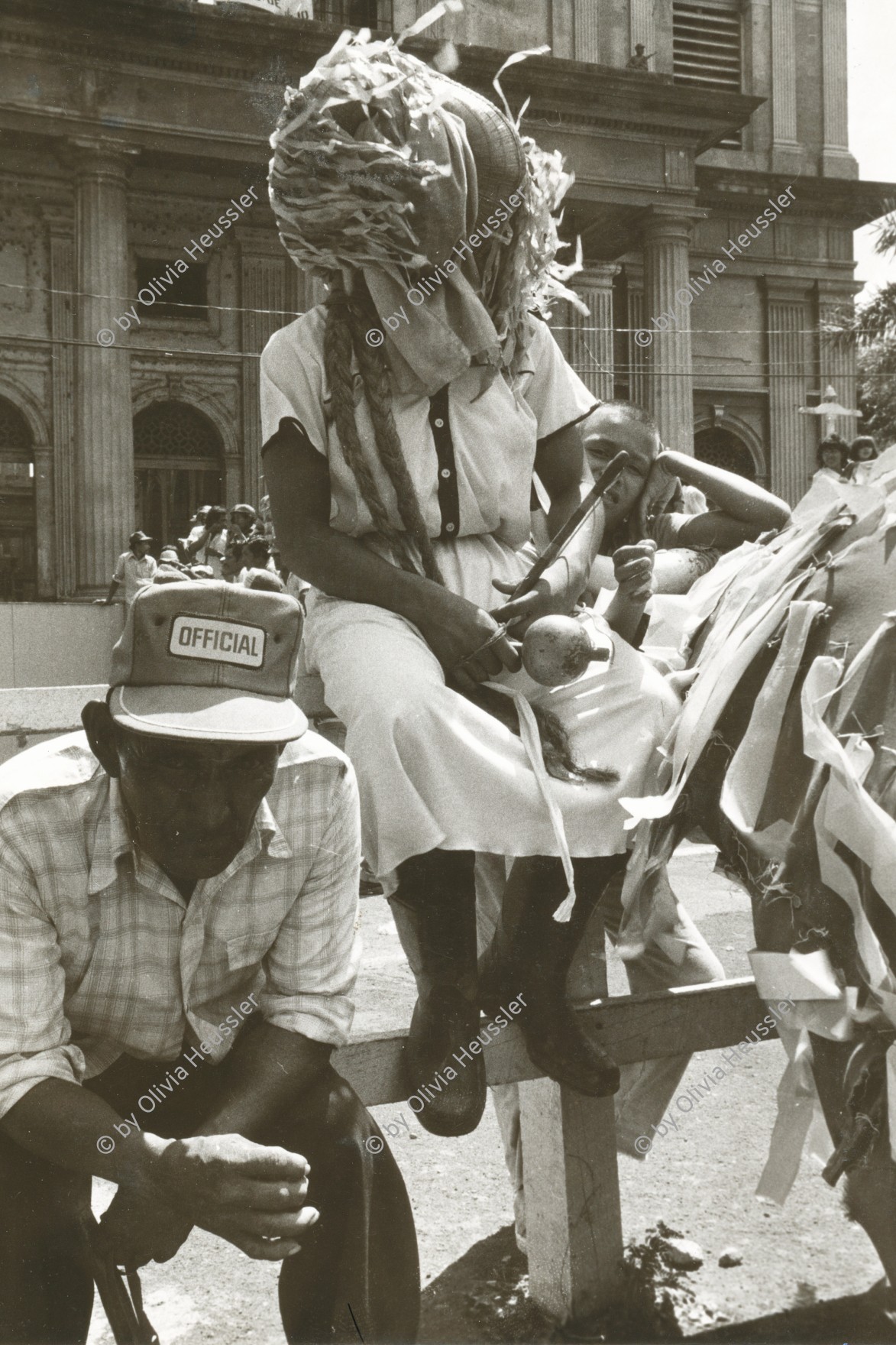 Image of sheet 19840610 photo 18: 'Lencho Catarran' Cataran Mann als Frau verkleidet. auf der Plaza de Gobierno. Cathedrale im Hintergrund. Demonstration. Bauern mit Masken Managua Nicaragua 1984 america central cultura culture theater √