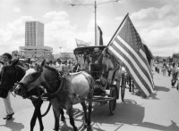 Image of sheet 19840610 photo 44: Nordamerikaner Innen unterstützen sandinistische Bauern der FSLN und der U.N.A.G. US-Amerikanische und Sandinistische Fahnen Flaggen nebeneinander. Banco de America und im vordergrund Demonstration. Bauern mit Masken und Pauke. Managua Nicaragua 1984