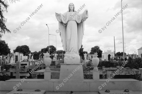 Image of sheet 19840650 photo 21: Das Grab von des sandinistischen Kommandanten der FSLN Cmdte. Enrique Schmidt auf dem Friedhof ist zerstört. Die Kränze liegen chaotische herum, im Cementerio General. Das Grab von Chamorro. Heiligenstatue. Kreuz. Kinderdemonstration. Kinder tragen Friedenstaube aus Karton. FSLN Fahnen. Panzer steht in Managua. Nicaragua 1984