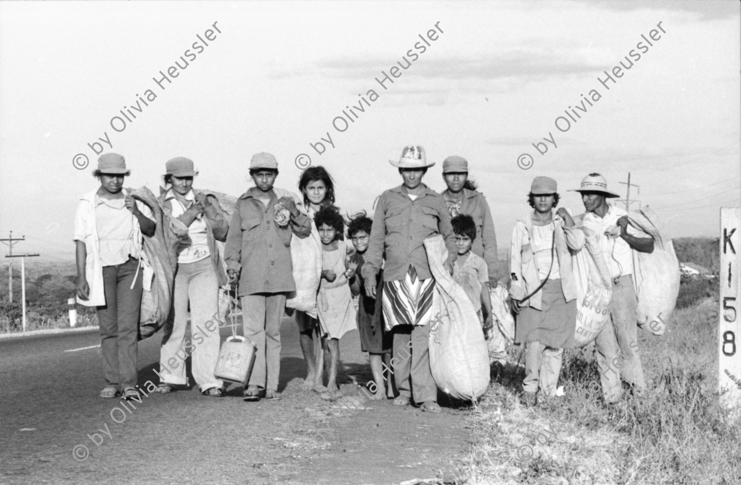 Image of sheet 19850040 photo 20: Frauen einer Kooperative ernten Baumwolle. Vulkan im Hintergrund. Sie gehen auf der Panamericana. Gruppenbild der Arbeiterinnen. Sie tragen Hüte die mit dem Namen Nicaragua bestickt sind. Eine Familie schleppt ein Wasser Wassertransport über die Landstrasse. Chinandega Nicaragua 1985