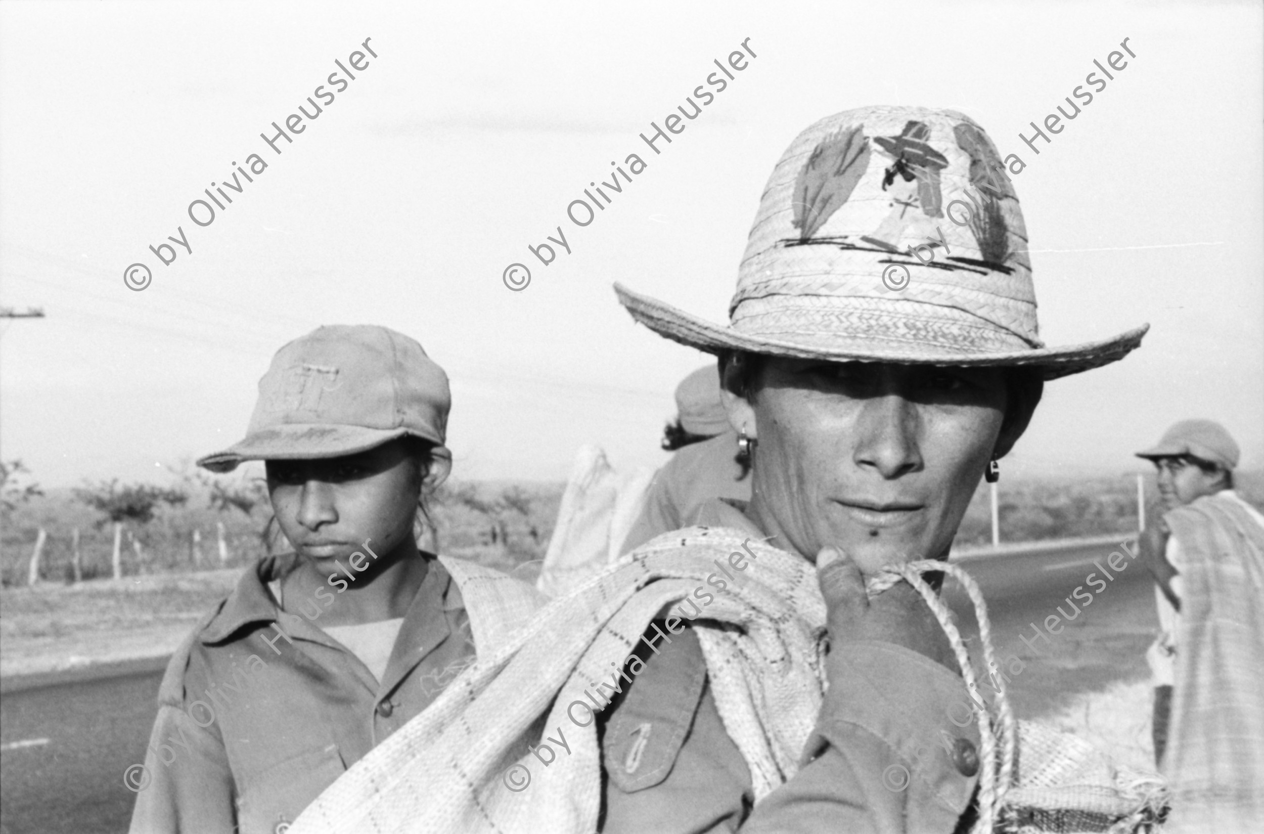 Image of sheet 19850040 photo 25: Frauen einer Kooperative ernten Baumwolle. Vulkan im Hintergrund. Sie gehen auf der Panamericana. Gruppenbild der Arbeiterinnen. Sie tragen Hüte die mit dem Namen Nicaragua bestickt sind. Eine Familie schleppt ein Wasser Wassertransport über die Landstrasse. Chinandega Nicaragua 1985