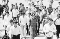 Image of sheet 19850120 photo 25: Gruppenbild der Kaffeebrigade. Abschied. Nica. Kameramann, Internationalistinnen Kaffeepflücker Brigade. Sängerin. sandinist Cmdte. Kommandant der Revolution Daniel Ortega spricht. im Hintergrund liegt Matagalpa. Kaffeesäcke. 
Product of Nicaragua libre. Lavado Segovia. Kaffee Nicaragua 1985 Arbeit Norma Elena Gadea singt.