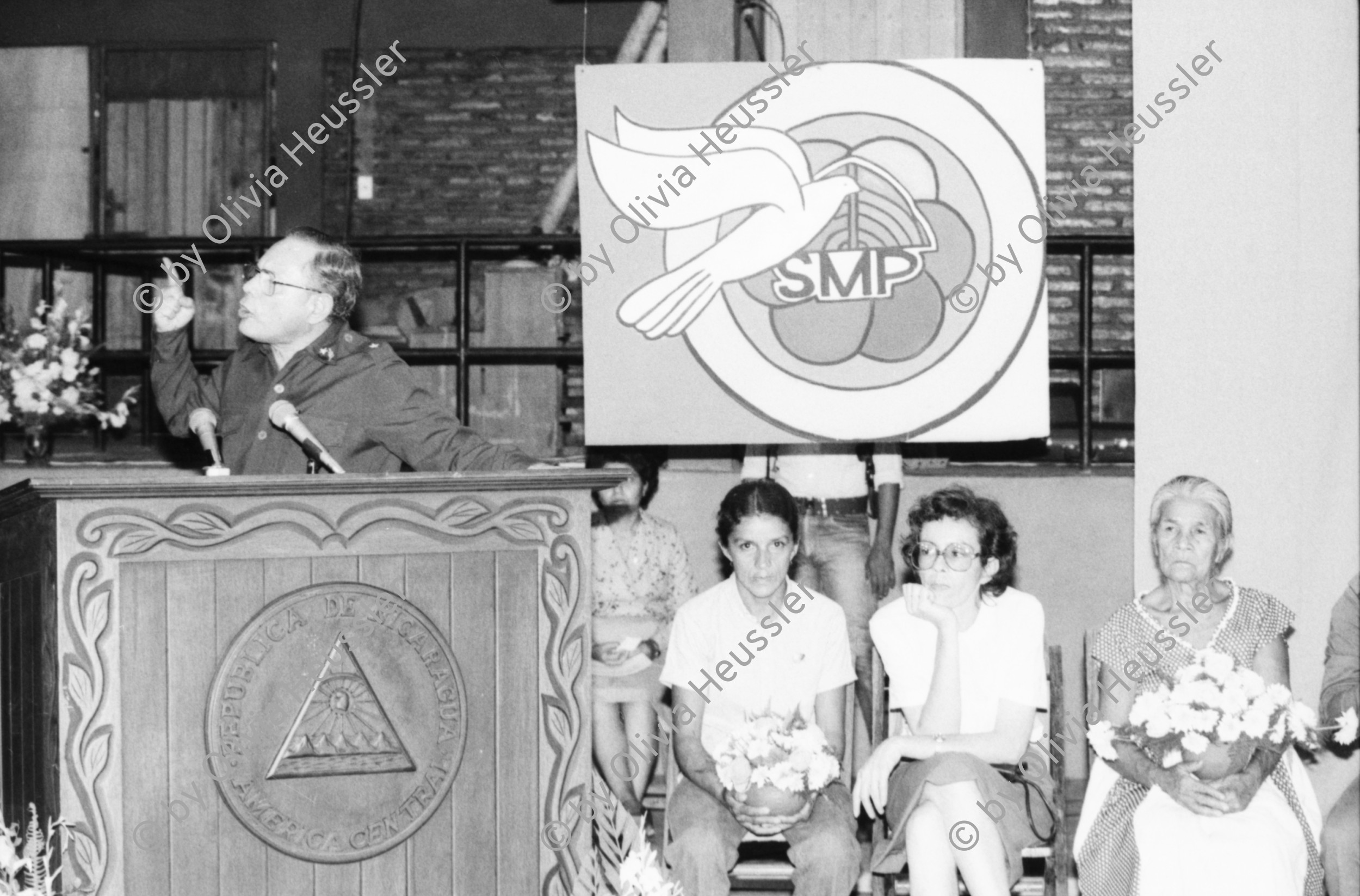 Image of sheet 19850130 photo 23: Kommandant Der sandinistische Sandinista Sandinismus Revolutions Comandante de la Revolucion Tomas Borge spricht für die Frauen der AMNLAE in Leon. Frauen schreien pol. Parolen. Propaganda für SMP. Hauswand aus ausgedienten alten Auto Nummernschilder Autoschilder Schilder. Willi Germund auf Baum sitzend in Xiloa. 2 kleine Kinder in Hängematte. Cornell (gest. in El Salvador, Holländer Kameramann für Jan Schmeitz) Gabriela Gabrielle Gabriel Baur und Peter Paul Zahl. (Schriftsteller; die Glücklichen, BRD Deutschland) liest aus dem anarchistischen Diabolik, Zürcher Untergrundmagazin aus Anarchokreisen. Beerdigung in Managua. Mutter von Luisa Amanda Espinoza mit Blumen. Nicaragua
1985