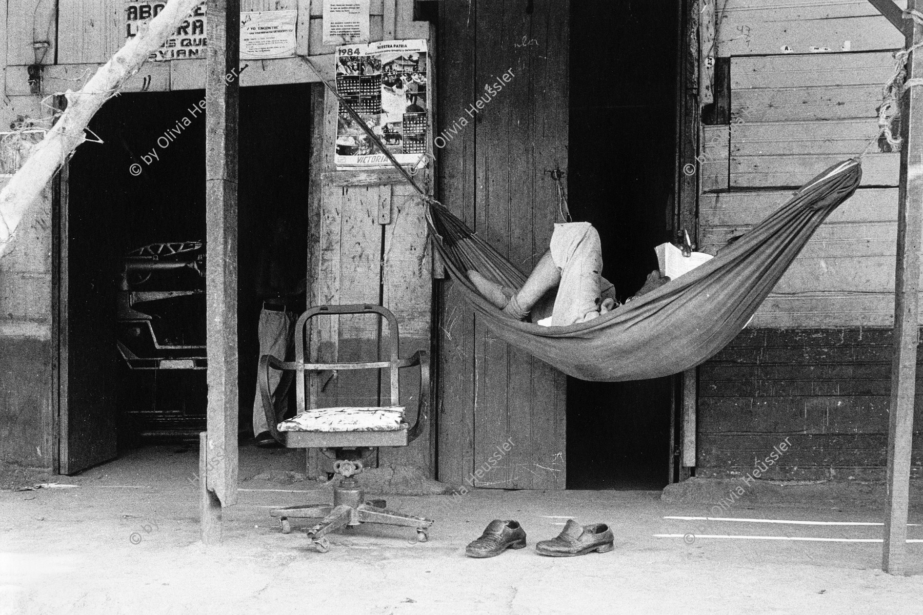 Image of sheet 19850140 photo 1: Noch sind die alten vor dem Erdbeben gebauten Häuser im Zentrum bewohnt. Sie sind aber als Ruinen zu bezeichnen. Sonntagnachmittag in Managua Nicaragua 1985 √ Mann man reading in hammock hamock Hängematte am lesen 
© 1985, by OLIVIA HEUSSLER / www.clic.li