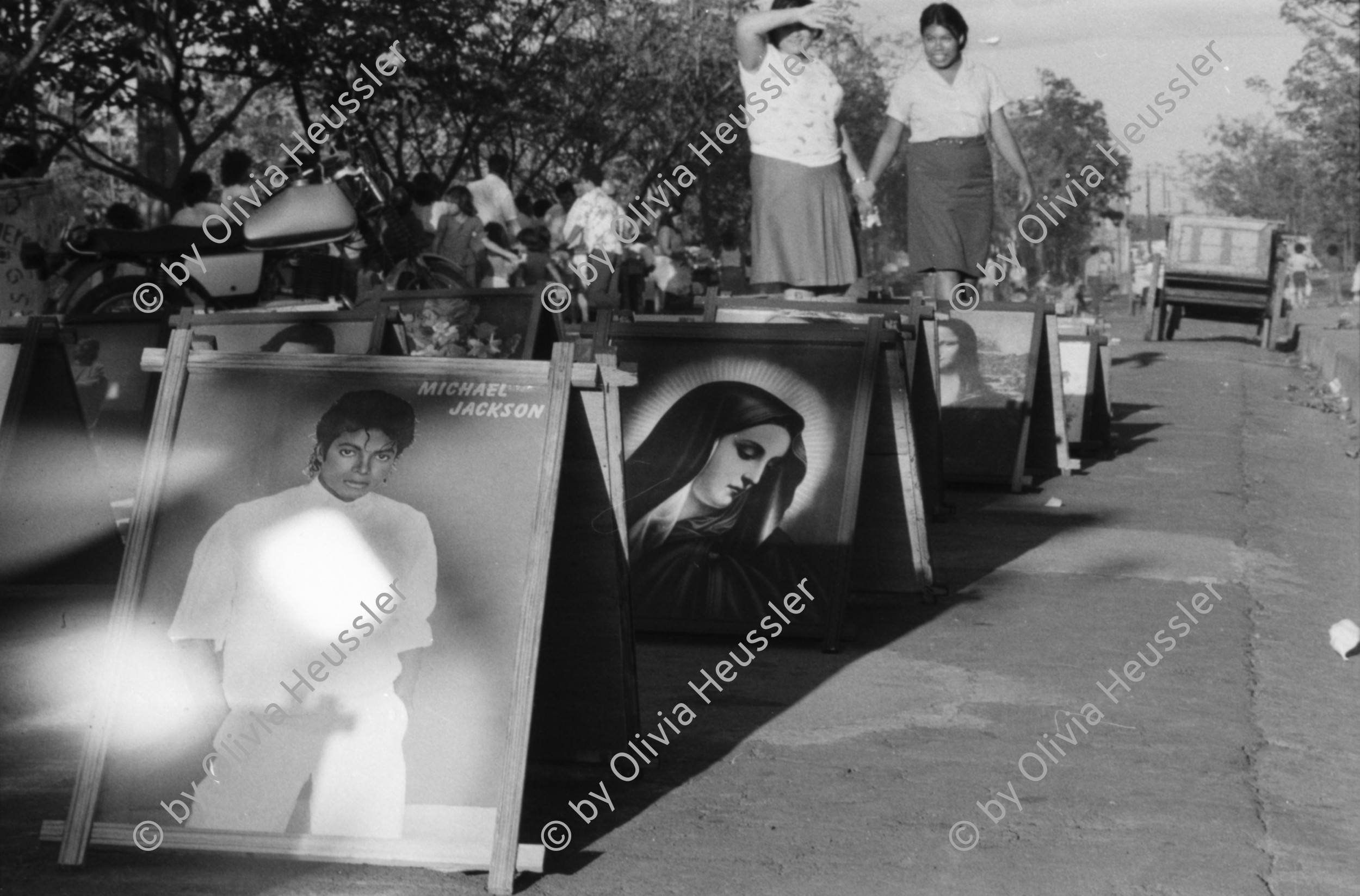 Image of sheet 19850140 photo 6: Der 2. Todestag der Salvadorianischen Kommandantin Ana Maria. Sie wurde in Nicaragua mit einer Axt erschlagen. Marcial, ihr Lebenspartner hat sich kurz darauf umgebracht. Verschiedene Junge Sandinisten stehen am Grab Wache Michael Jackson und die Jungfrau Maria sind begehrte Objekte. Die importierten Plakate sind sehr populär. Junge vor alem Alter Tank gepanzertes Militärfahrzeug steht heute im vom Erdbeben zerstörten alten Managua wo die Kinder spielen. Noch sind die alten vor dem Erdbeben gebauten Häuser im Zentrum bewohnt. Sie sind aber als Ruinen zu bezeichnen. Korbball. Basketball am Sonntagnachmittag. Nicaragua 1985