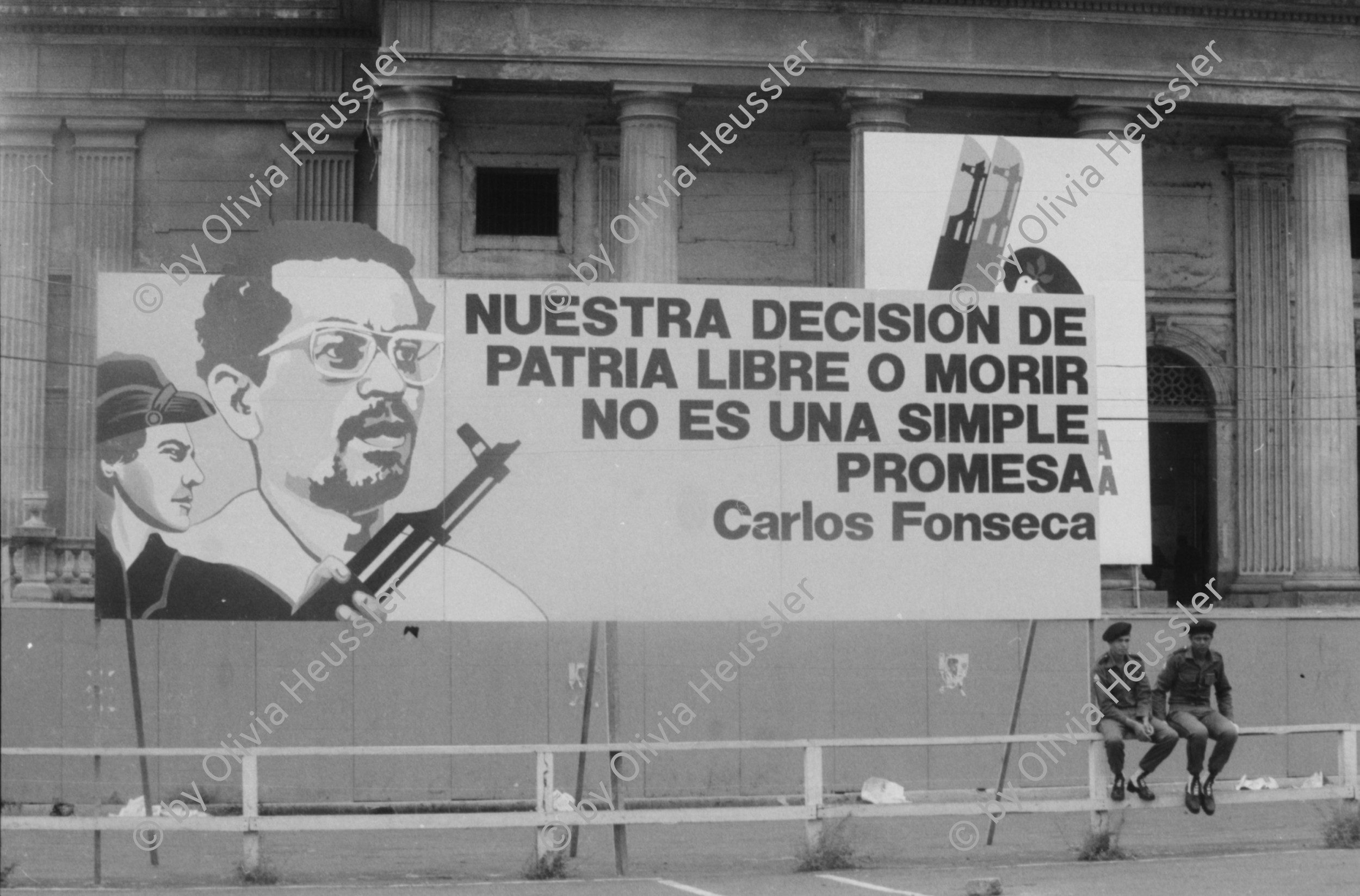 Image of sheet 19850360 photo 17: Auf dem Platz vor dem National Palast Plaza de la Revolution, stehen tausende von sandinistischen Soldaten sandinistischer sandinisten EPS bereit für ein Abtreten. demobilisation. Humberto Ortega spricht an sie. US Amerikanische Militäroffiziere fotografieren uns  Journalisten Das Monument für die Bauern Campesinos mit der Kalaschnikov AK 47  in Managua wird bald der Oeffentlichkeit übergeben und vom Gerüst befreit. 
'Nuestra descision de patria libre o morir no es una simple promesa'. Carlos Fonseca.Unsere Entscheidung ob Freies Vaterland oder Tod ist nicht nur eine einfache Voraussagung. einfaches Versprechen. Sechs Jahre Revolution. Das siegreiche Nicaragua verkauft und ergibt sich nicht! Militärparade Managua Nicaragua 1985