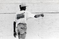 Image of sheet 19850370 photo 17: Ein junger Mann in abgeschnittenen Jeans bepinselt bemalt sein Haus mit weisser Farbe. Auf seinem Rücken trägt er die Farben Rot und Schwarz. Sie sind die Propagandafarben für die Sandinisten FSLN zu den Wahlen. San Juan del Sur Nicaragua 1985 √
