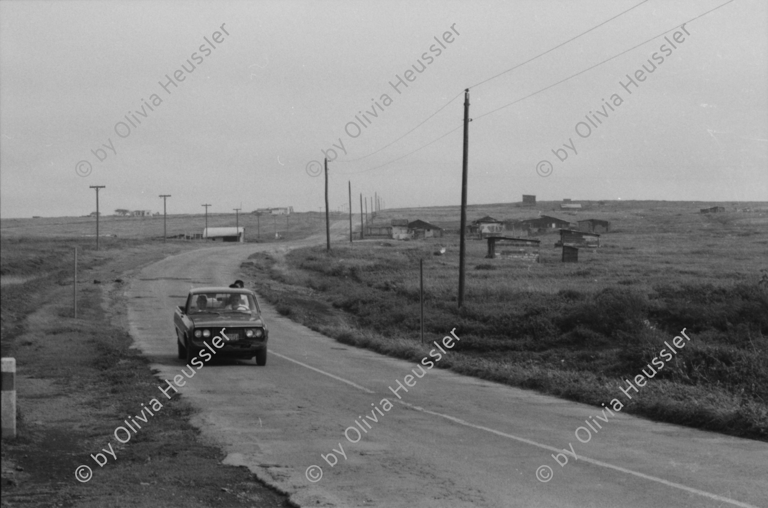Image of sheet 19850440 photo 19: Am frühen Morgen fahre ich nach El Crucero . Es liegt hoch über Managua und es liegt immer im Nebel des Schwefeldampfes vom Vulkan Masaya. es ist ein paar Grade kühler dort. Der Schwefeldampf vom Vulkan in  Masaya, dem Santiago macht es der Natur unmöglich zu gedeihen. Bäume und andere Pflanzen ertragen
diese Luft nicht. Trotzdem stehen da einige Häuser und vereinzelt sehe ich Menschen. Frau mit Rind Kinder stehen da. Ein Mädchen vor einer Bretterwand Haus. Wandmalereien. COSEP Leute an PK.
José Chepe auf Motorrad Trautes. Gruppenbild Carretera sur. Managua 1985