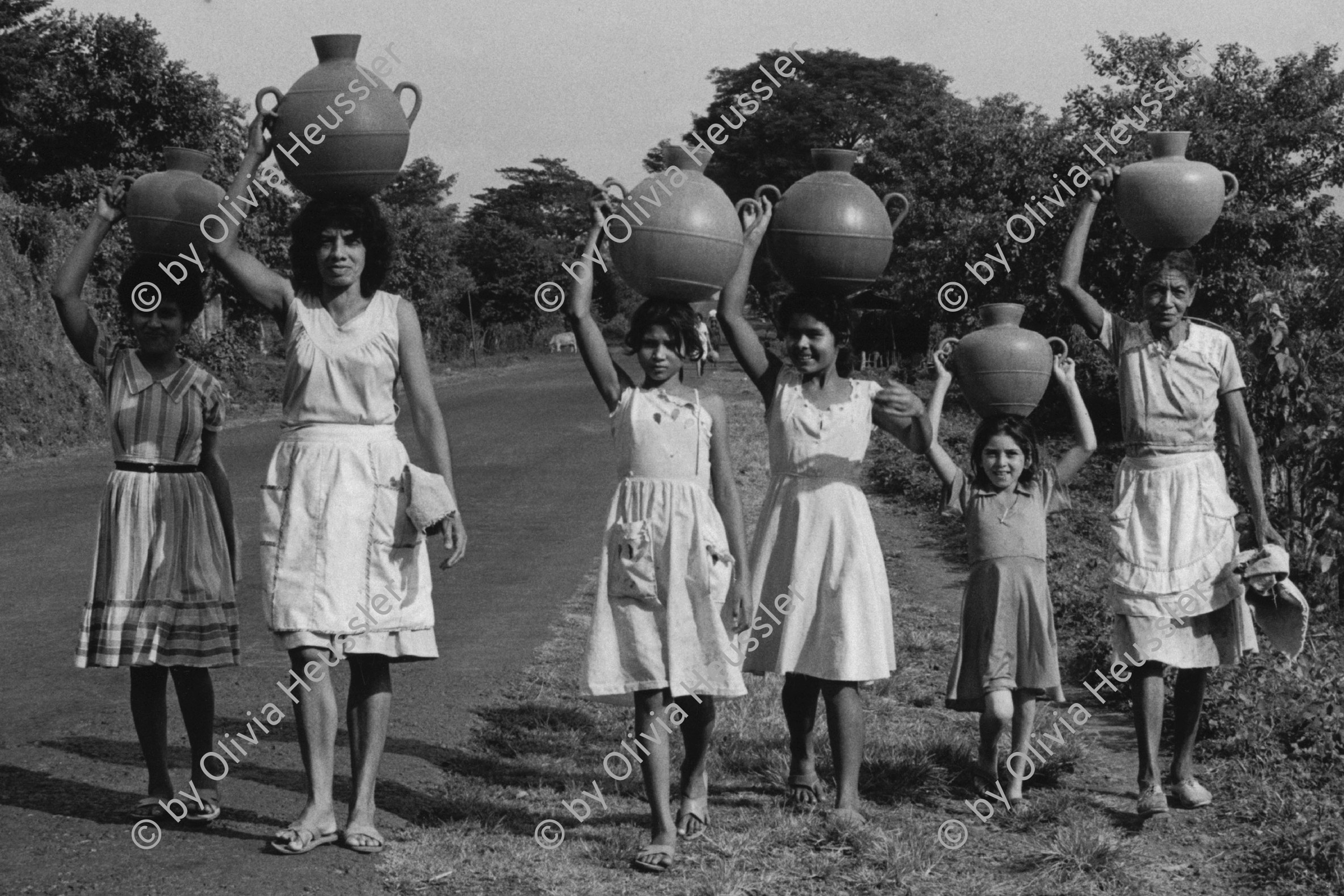 Image of sheet 19850471 photo 11: Frauen in allen Generationen (Mütter, Kinder und Jugendliche) tragen transportieren Wasserkrüge aus Plastik PVC auf dem Kopf. Panamericana. El Salvador 1985 pottery plastic water transport women child tanks 
Zentralamerika Centralamerica El Salvador 1985 √
Gruppenbild
© 1985, OLIVIA HEUSSLER / www.clic.li
